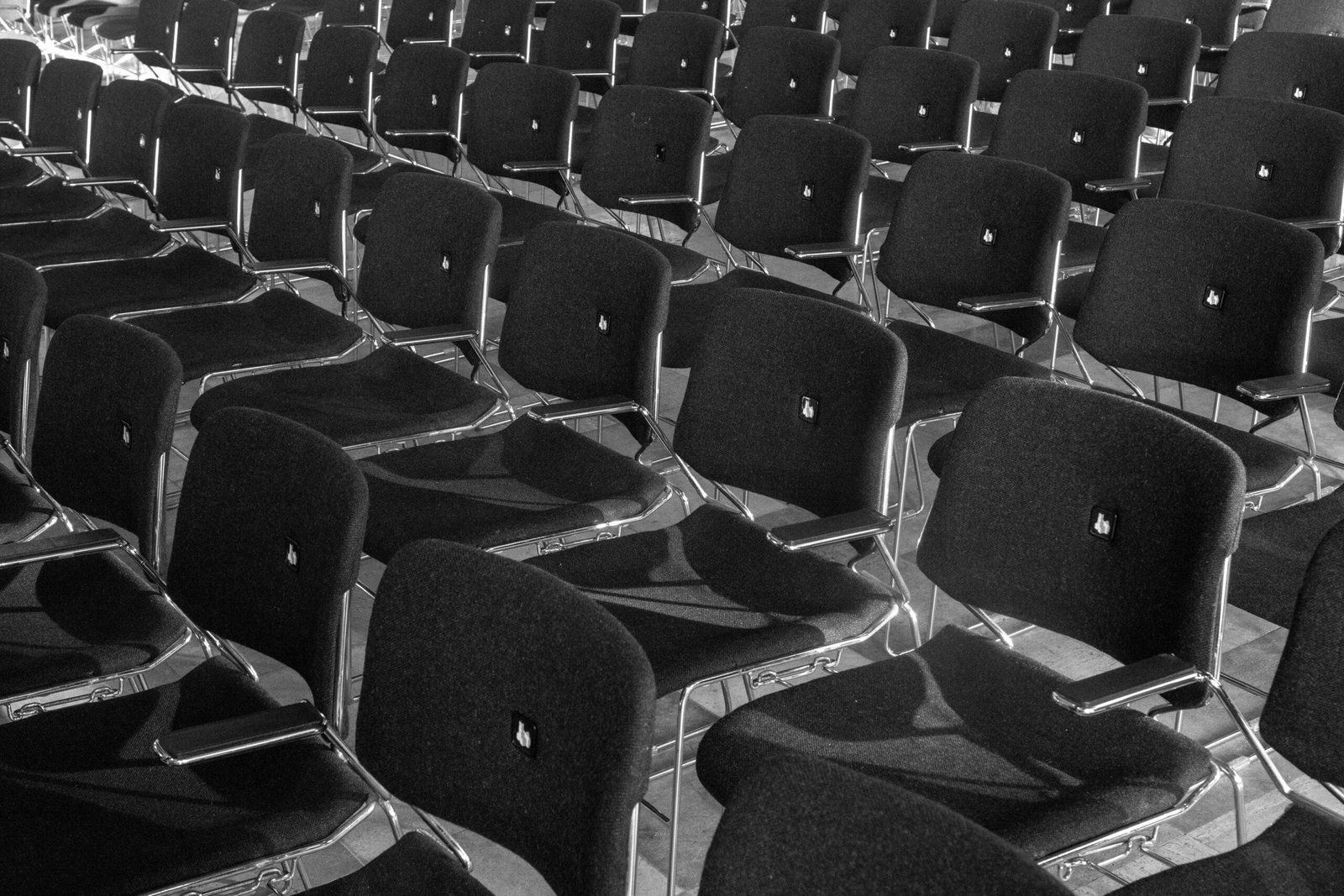 Black and white photo of aligned empty chairs in a conference or auditorium setting.